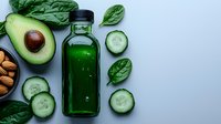 Green detox juice in glass bottle surrounded by fresh cucumber slices, spinach leaves, avocado and almonds on light background. Healthy eating concept.