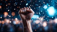 Raised black fist silhouette against blurred bokeh lights background symbolizing unity, strength, and social movement. Dramatic urban nighttime atmosphere.