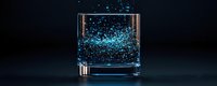Glowing blue particles suspended in clear liquid inside glass tumbler on dark background, creating magical luminescent effect for beverage photography.