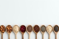 Wooden spoons filled with diverse superfoods and seeds including almonds, quinoa, cranberries, chia, coffee beans and poppy seeds arranged in row on white background.