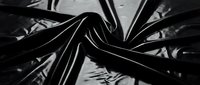 Glossy black vinyl material with dramatic folds and creases creating abstract sculptural forms against dark background for fashion and textile design.