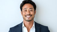 Confident Asian businessman in navy suit and white shirt smiling warmly against light background, showcasing professional leadership and success in corporate setting.