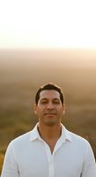 Middle-aged man with dark hair and olive complexion wearing white button-up shirt, photographed outdoors during golden hour with soft blurred background for portrait and lifestyle use.