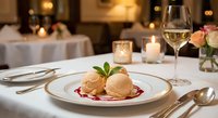 Elegant gourmet dessert with vanilla ice cream and berry sauce served on white plate in upscale restaurant dining room with candlelight and wine glass.