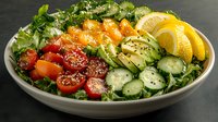 Fresh poke bowl with salmon, avocado, cucumber, cherry tomatoes, and citrus on green lettuce bed, garnished with sesame seeds in gray ceramic bowl.