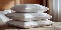 Stack of three white fluffy pillows on wooden floor in sunlit room creating cozy bedroom atmosphere for home decor and comfort concepts.