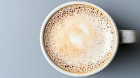 Frothy cappuccino with delicate milk foam bubbles in gray ceramic cup on light background, top view. Fresh morning coffee with creamy heart pattern.