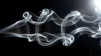 Elegant white smoke swirls flowing gracefully against a dark black background, creating abstract curling wave patterns with soft light effects.