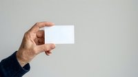 Close-up of male hand holding blank white business card against neutral background. Suitable for corporate branding, identity design, and marketing materials.