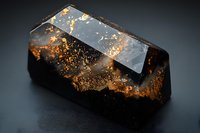 Black crystal with golden inclusions on dark background, dramatic lighting highlights natural mineral formation with metallic copper-colored patterns and geometric facets.