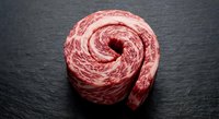 Raw ground beef meat formed in spiral shape on dark slate surface for culinary preparation and cooking recipes.