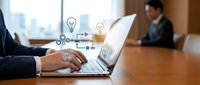 Business professional using laptop with creative innovation icons floating above screen in modern office meeting room setting.