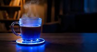 Steaming blue herbal tea in transparent glass mug on wooden table with warm ambient lighting creating cozy atmosphere for relaxation and wellness.