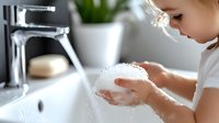 Young girl washing hands with soap and water at bathroom sink, demonstrating proper hygiene habits and cleanliness routine in bright modern setting.
