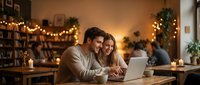 Young couple using laptop together at home with warm Christmas lights creating cozy romantic atmosphere for holiday online shopping or planning.