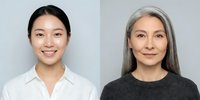 Two professional women of different ages and ethnicities smiling at camera against neutral background for business portraits and corporate headshots.