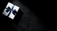 White gift box with dark blue ribbon bow on black background, isolated for holiday greeting cards, promotional materials, and festive design projects.