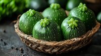 Fresh round green zucchini squash in rustic woven basket on dark background, close up view of organic seasonal vegetables with textured skin.