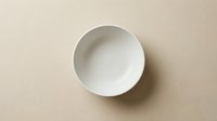Empty white ceramic bowl on neutral beige background, overhead view. Isolated tableware for dining, kitchen, restaurant, and food styling design projects.