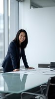 Confident Asian businesswoman in navy suit leaning over glass conference table reviewing documents in modern office meeting room.