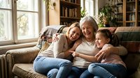 Three generations of Caucasian women laughing together on a cozy sofa at home, grandmother, mother and granddaughter sharing a joyful family moment.