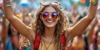 Young woman with curly hair and sunglasses celebrating at music festival, arms raised in joy, colorful crowd in background.