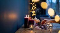 Cozy evening scene with burning candles, warm bokeh lights, and hands arranging festive decorations on wooden table creating intimate holiday atmosphere.