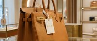 Luxury tan leather handbag with gold hardware and sale tag displayed in an upscale boutique, showcasing premium fashion retail shopping.