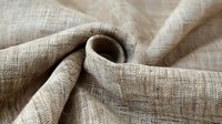 Natural linen fabric with textured weave pattern in beige color showing folds and wrinkles, raw organic material for sustainable fashion and home decor.