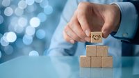 Businessman placing wooden block with smiley face on top of pyramid stack, representing customer satisfaction, positive feedback, and business growth strategy.