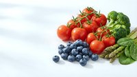 Fresh organic vegetables and berries on white background including cherry tomatoes, broccoli, blueberries, asparagus and spinach for healthy eating.