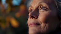 Mature Caucasian woman's face in golden sunset light, eyes closed peacefully with natural wrinkles and gentle smile showing contentment and serenity in outdoor setting.