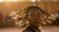 Young African woman with traditional braided hairstyle in golden sunlight creating dramatic backlighting effect for cultural diversity and beauty concepts.