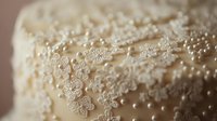 Delicate lace-like sugar pearls cascade across cream-colored wedding cake surface, creating elegant pattern with soft focus and romantic macro details.