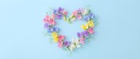 Colorful sweet pea flowers arranged in a heart shape on a pastel blue background, celebrating love, spring, and romance.