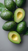 Fresh ripe avocados with green textured skin and creamy flesh halves arranged on gray background with leaves, top view food photography.