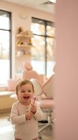Happy toddler girl holding pink toothbrush in modern dental office with chair and equipment in background for pediatric dentistry and oral health.