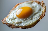 Close-up macro shot of sunny side up fried egg with crispy brown edges and bright yellow yolk on neutral background, showcasing texture and detail in food photography.