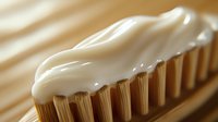 White toothpaste squeezed onto brown bristles of toothbrush in macro photography, morning hygiene routine with soft natural lighting and creamy texture.