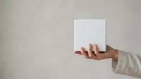 Person with medium skin tone holding blank white card or canvas against neutral background, suitable for mockups, presentations, and advertising campaigns.