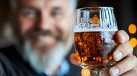 Man holding glass of craft beer with foam head and bubbles against blurred background with bokeh lights, close-up view focused on amber beverage.