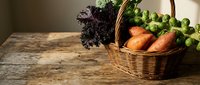 Fresh organic vegetables in wicker basket on rustic wooden table, including carrots, Brussels sprouts and kale for healthy cooking and farm-to-table concepts.