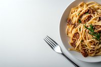 Traditional spaghetti bolognese pasta with minced meat sauce and parmesan cheese garnished with fresh herbs on white ceramic plate, fork beside.