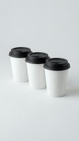 Three white disposable coffee cups with black lids arranged in row on neutral background, takeaway beverage containers for cafe and restaurant branding.