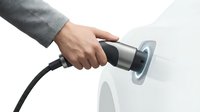 Hand holding electric vehicle charging cable plugging into white car port for sustainable transportation and eco-friendly automotive technology.