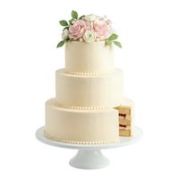 Elegant three-tier wedding cake with cream frosting, pearl piping details, and fresh pink and white roses on top, displayed on white cake stand with slice removed.