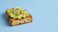 Avocado toast topped with crushed red pepper flakes on artisan bread slice against blue background for healthy breakfast menu design.