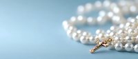 Elegant pearl rosary beads with golden cross lying on soft blue background, spiritual prayer accessory with selective focus and copy space.