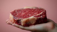 Raw ribeye steak with marbling held in palm against pink background, showcasing fresh meat texture and quality for food photography and culinary marketing.