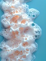 Creamy white foam with peach and blue bubbles flowing across turquoise background, creating abstract fluid texture for cosmetic or spa design.
